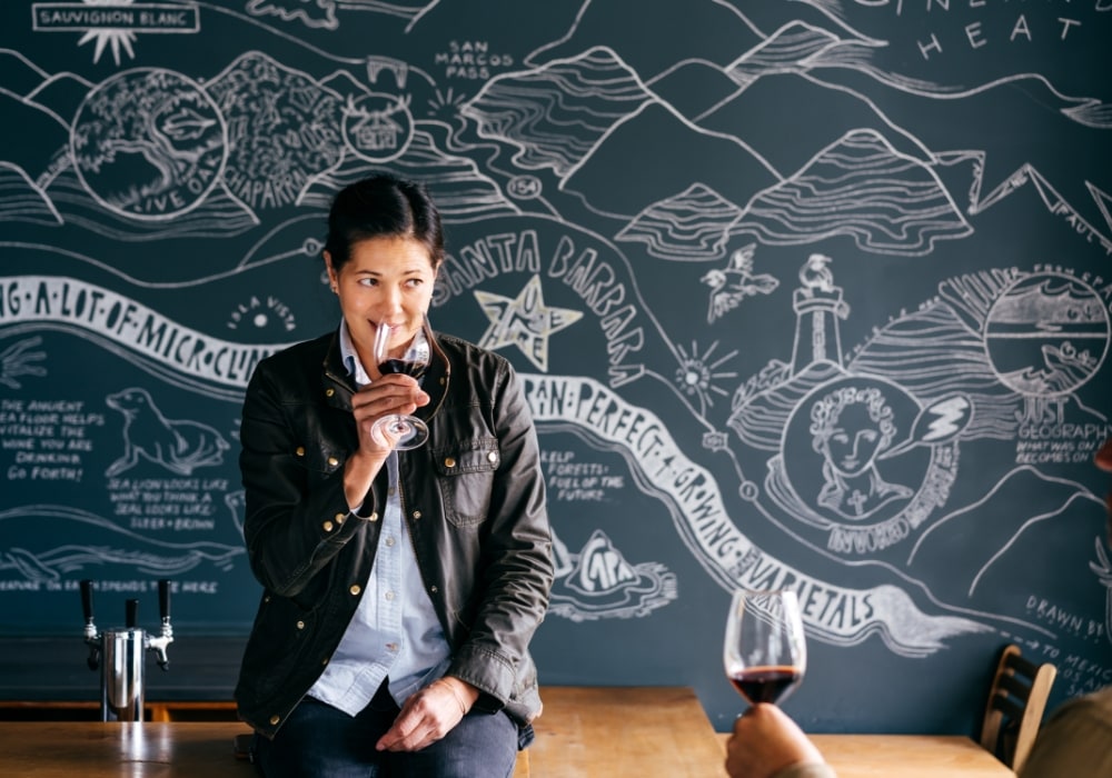lady sipping wine in front of a blackboard