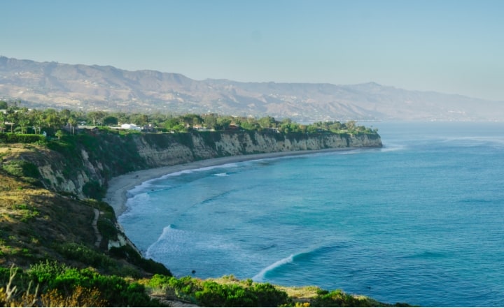 Ariel view of the north coast of California, white cliff sides and blue ocean and mountains in the background.