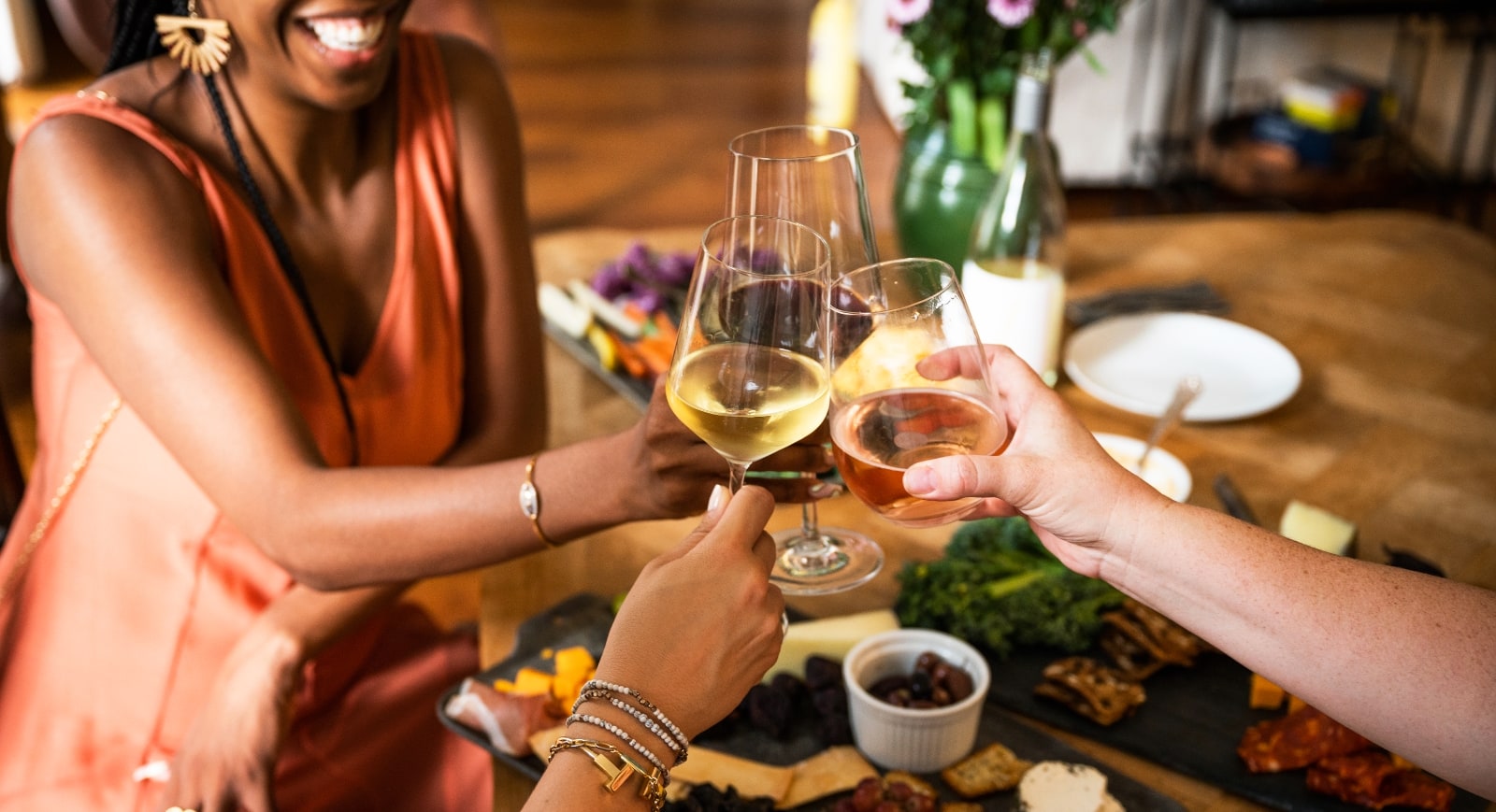 Three people raising their wine glasses around a dinning table.