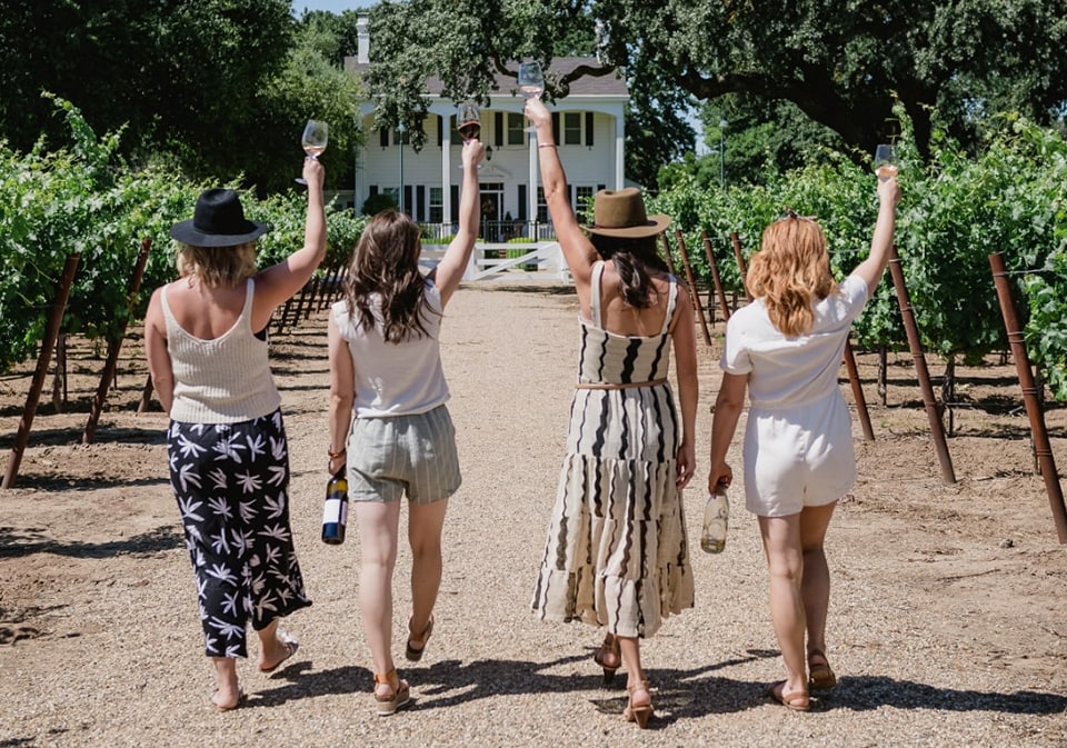 four people holding up wine glasses as they walk away